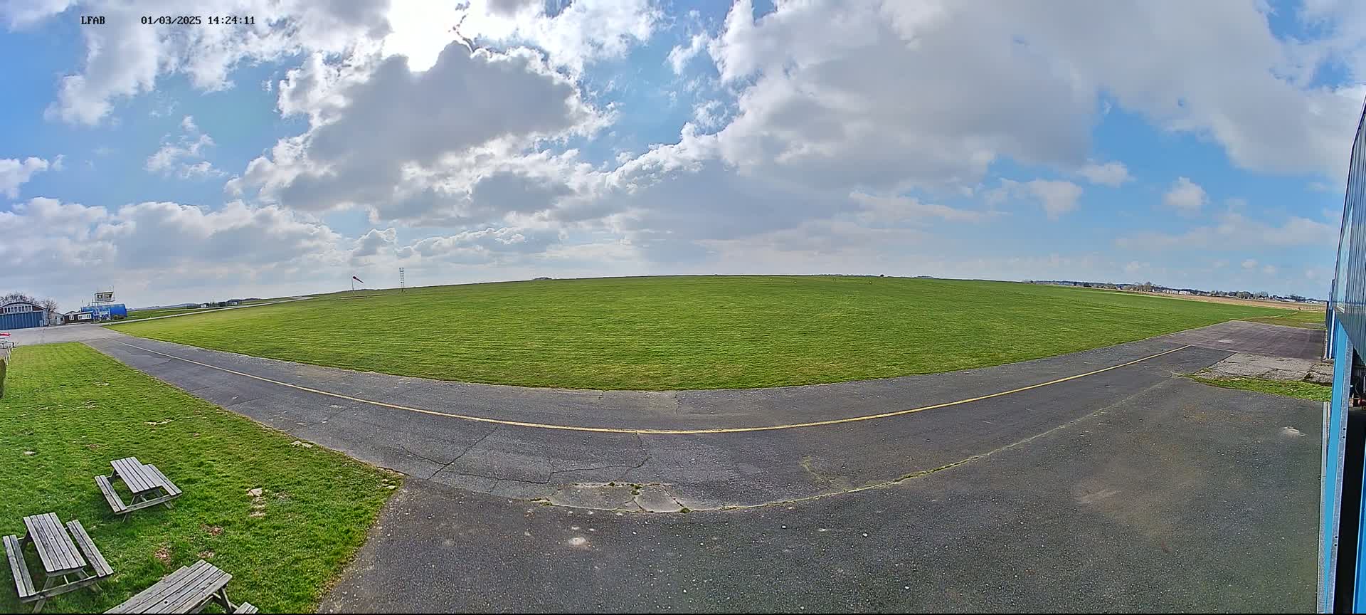 A paved taxiway curves around a grassy airfield under a partly cloudy sky.