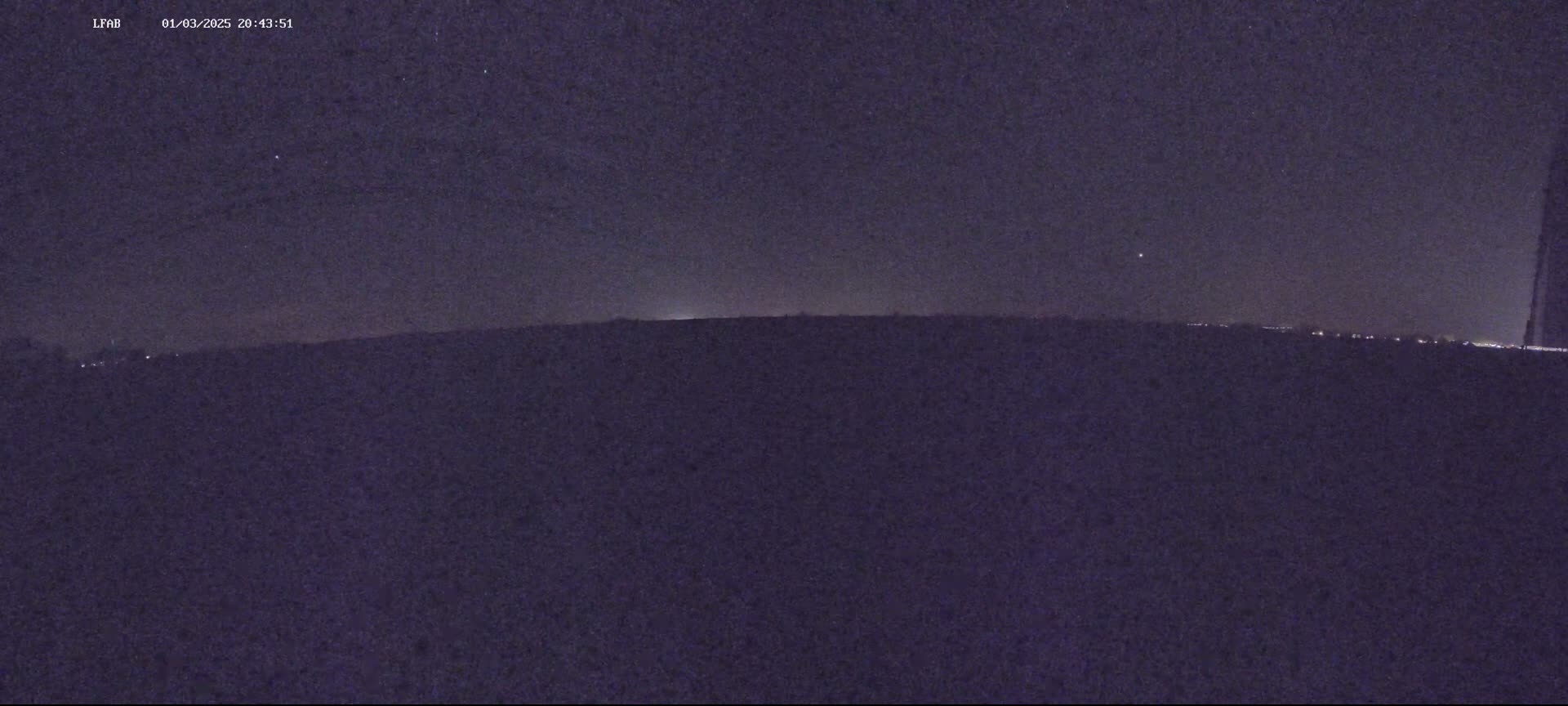 A nighttime, low-light view shows a dark, flat landscape under a starlit sky.
