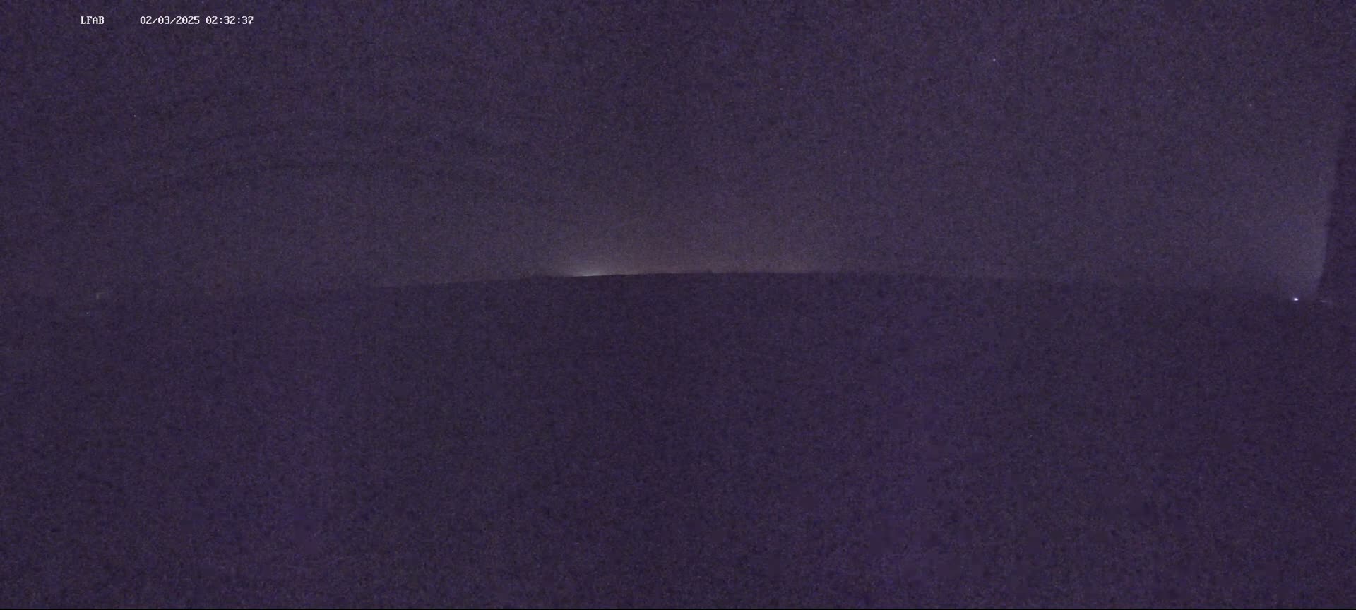 A dark, nighttime landscape is visible, with a faint light source on the horizon.