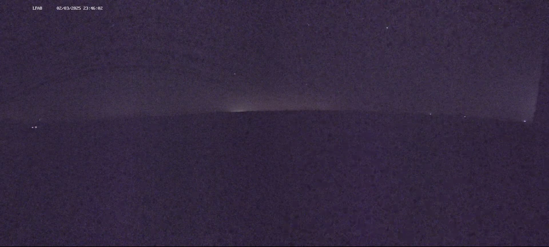 A dark, nighttime landscape is visible under a mostly clear, starry sky, with a faint light source on the horizon.