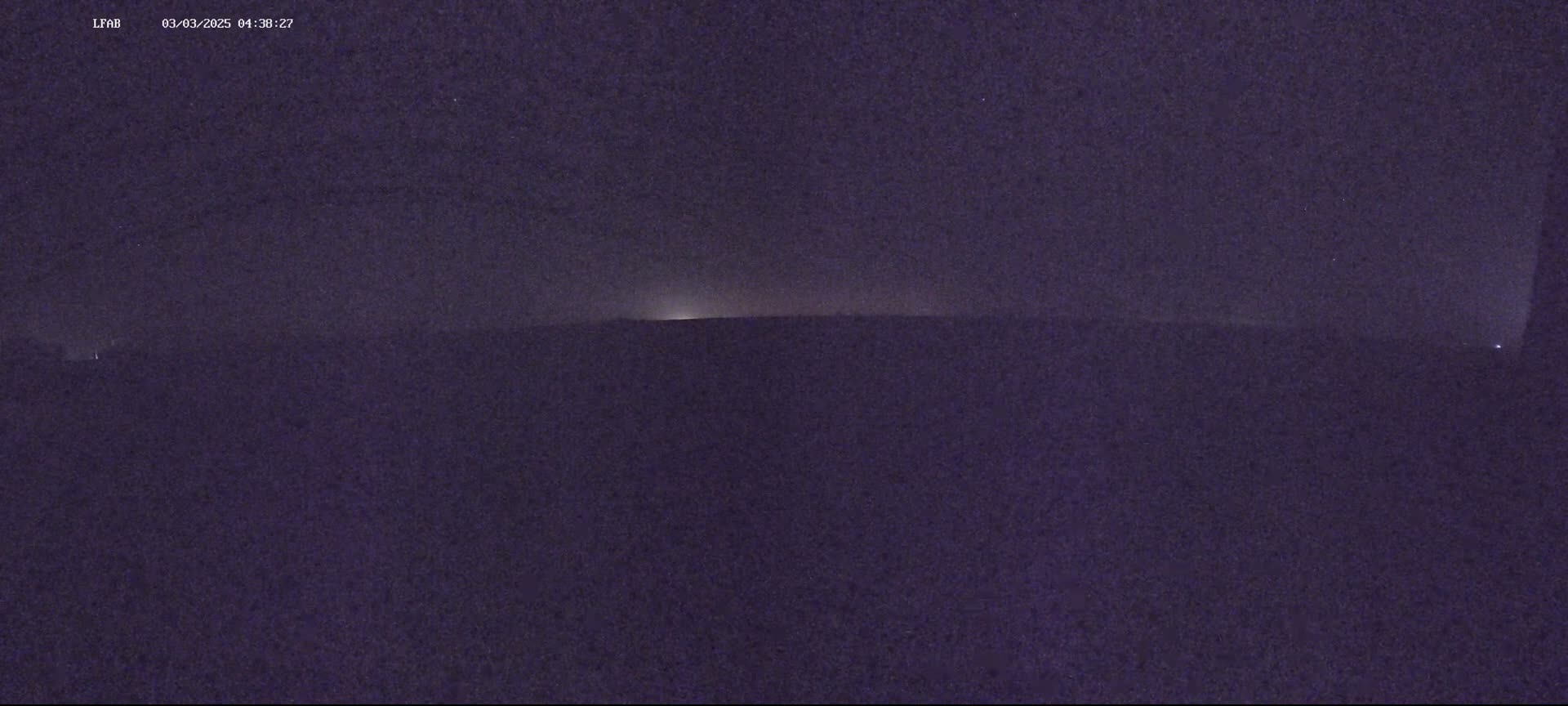 A dark, hazy night scene shows a flat horizon line with a faint glow on the horizon.