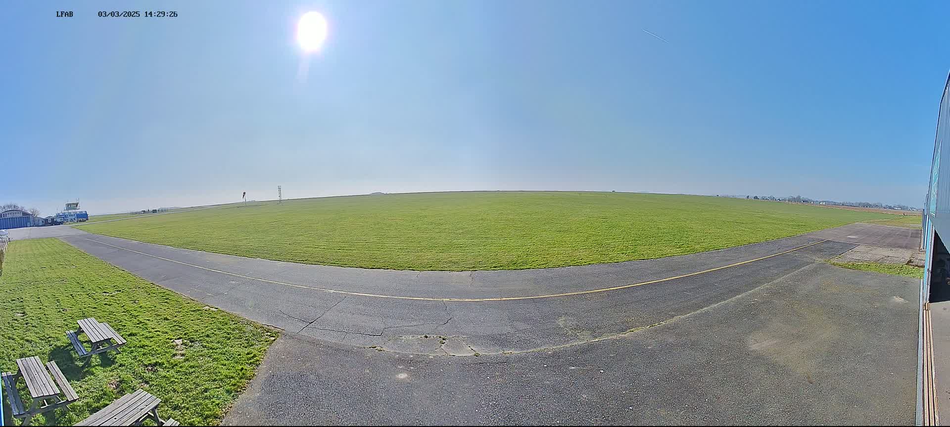 A paved taxiway curves through a grassy airfield under a bright, sunny sky.