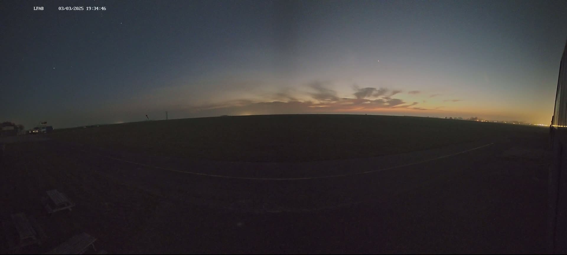 A dark, flat landscape is visible under a twilight sky with thin clouds exhibiting warm colors near the horizon.
