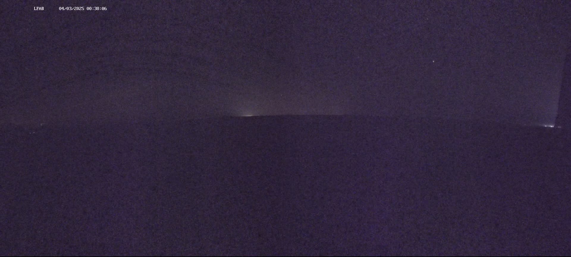 A dark, nighttime scene shows a dimly lit horizon under a mostly clear sky.