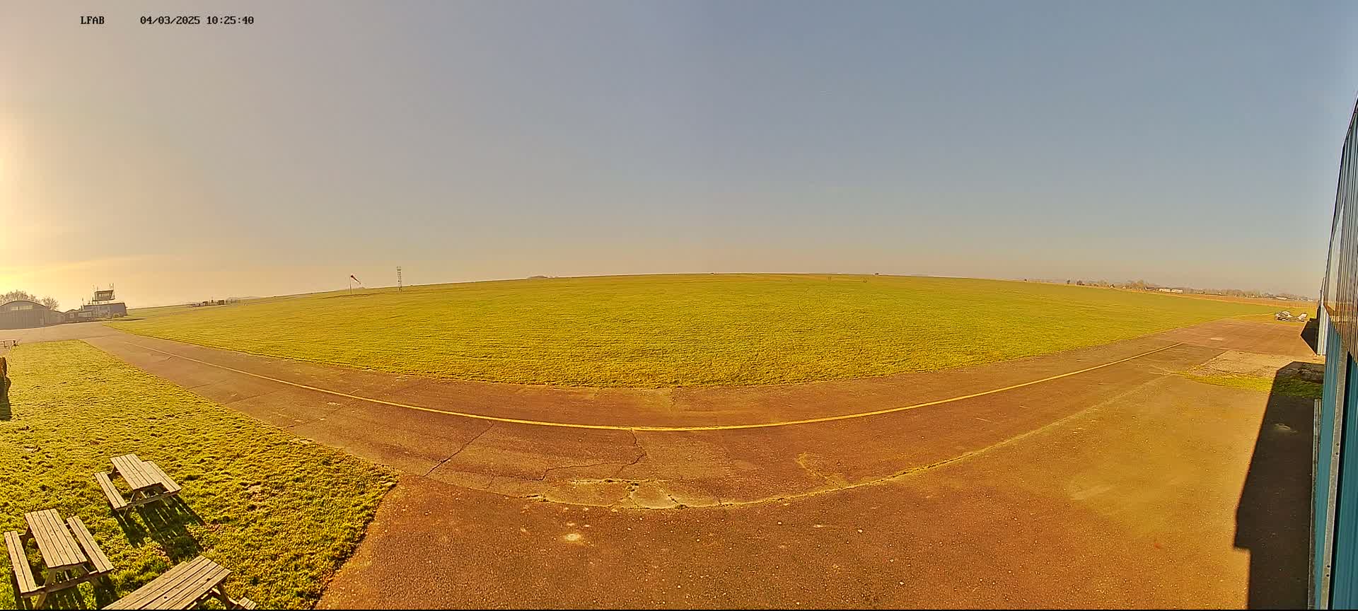 A paved taxiway curves through a grassy airfield on a sunny day.