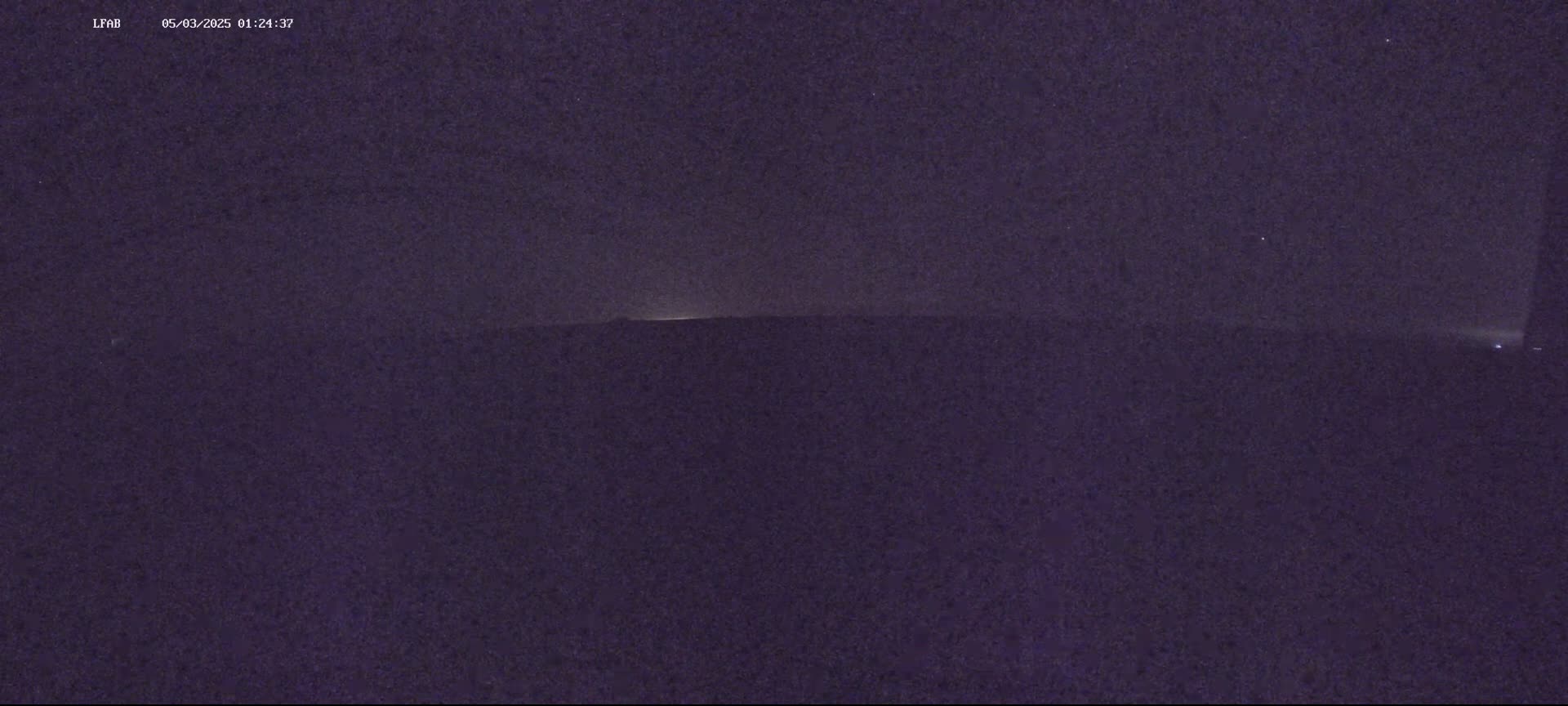 A dark, nighttime scene shows a flat, dark landscape with a faintly illuminated horizon under a clear, star-filled sky.