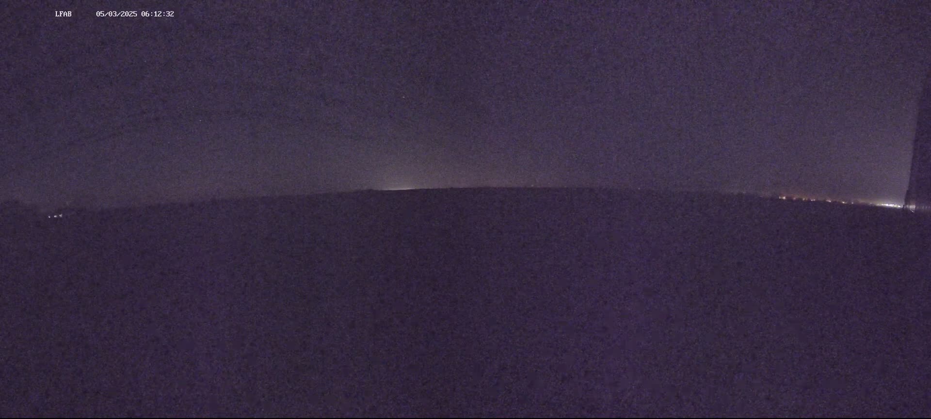 A dark, nighttime landscape is visible, with a faint horizon line and a few distant lights.