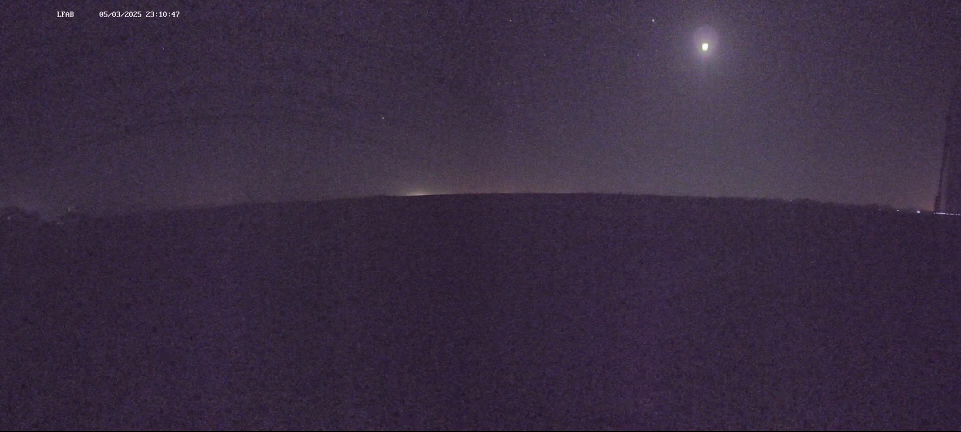 A bright light is visible in the night sky above a dark, flat horizon.