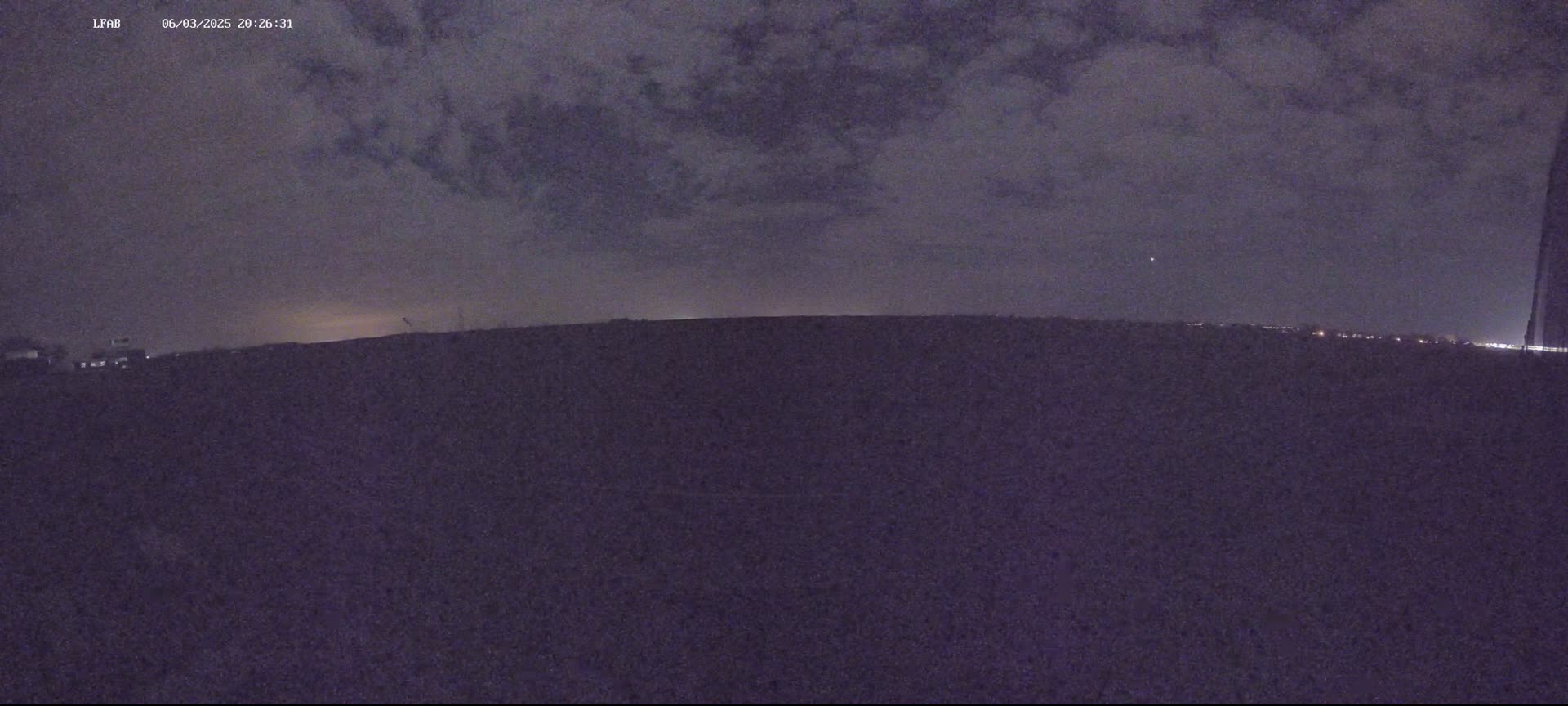 A dark, flat landscape is visible under a mostly cloudy night sky.