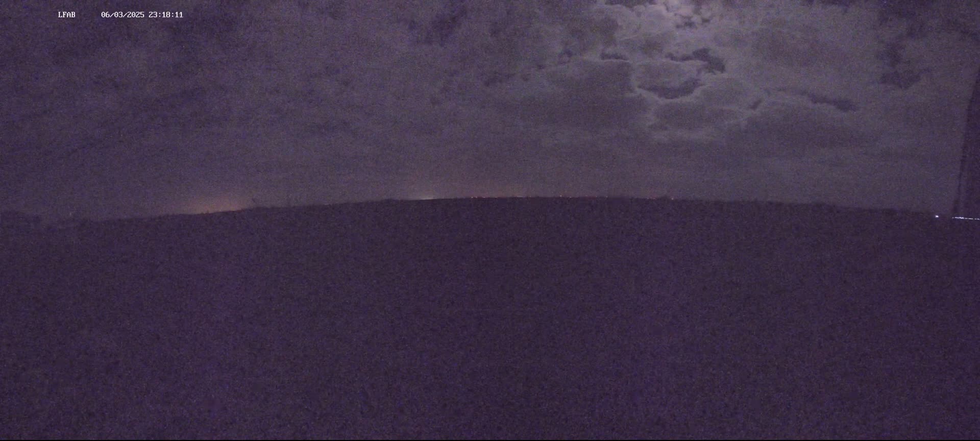 A dark, nighttime landscape is shown under a cloudy sky with a faint horizon line visible.