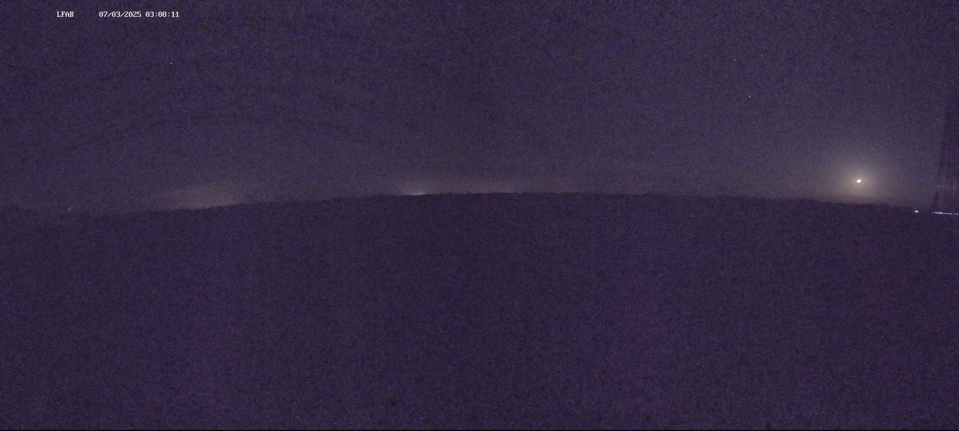 A dark, nighttime landscape shows a dimly lit horizon with a bright moon in the upper right corner of the frame.