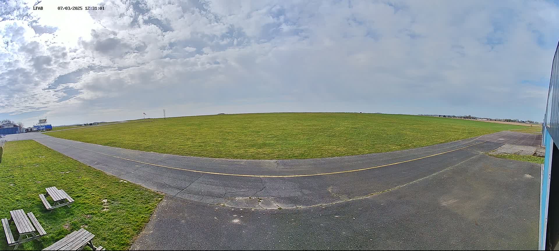 A paved taxiway curves through a grassy airfield under a partly cloudy sky.