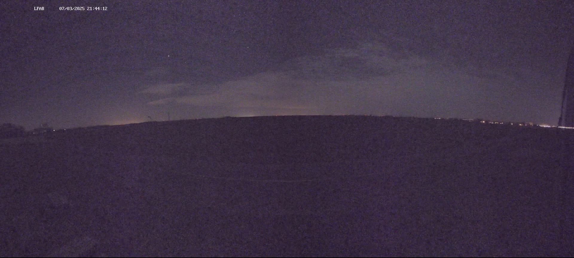 A dark, flat landscape is visible under a night sky with a thin layer of clouds.