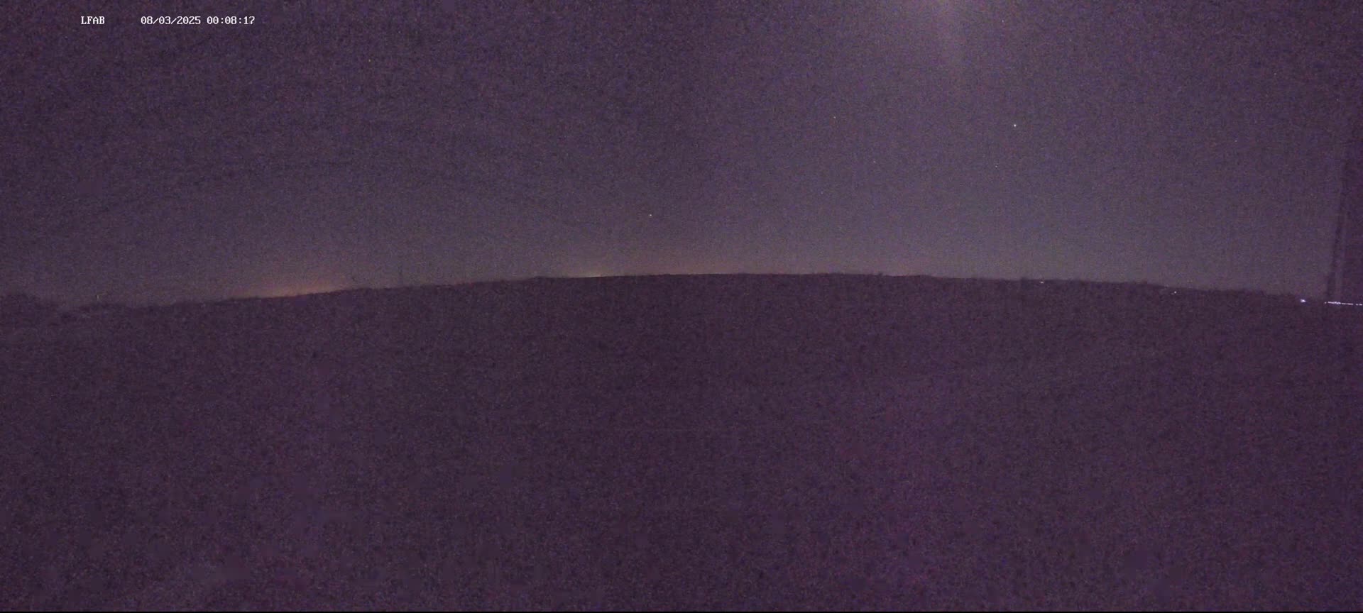 A dark, nighttime landscape shows a flat horizon line under a mostly clear, starlit sky.