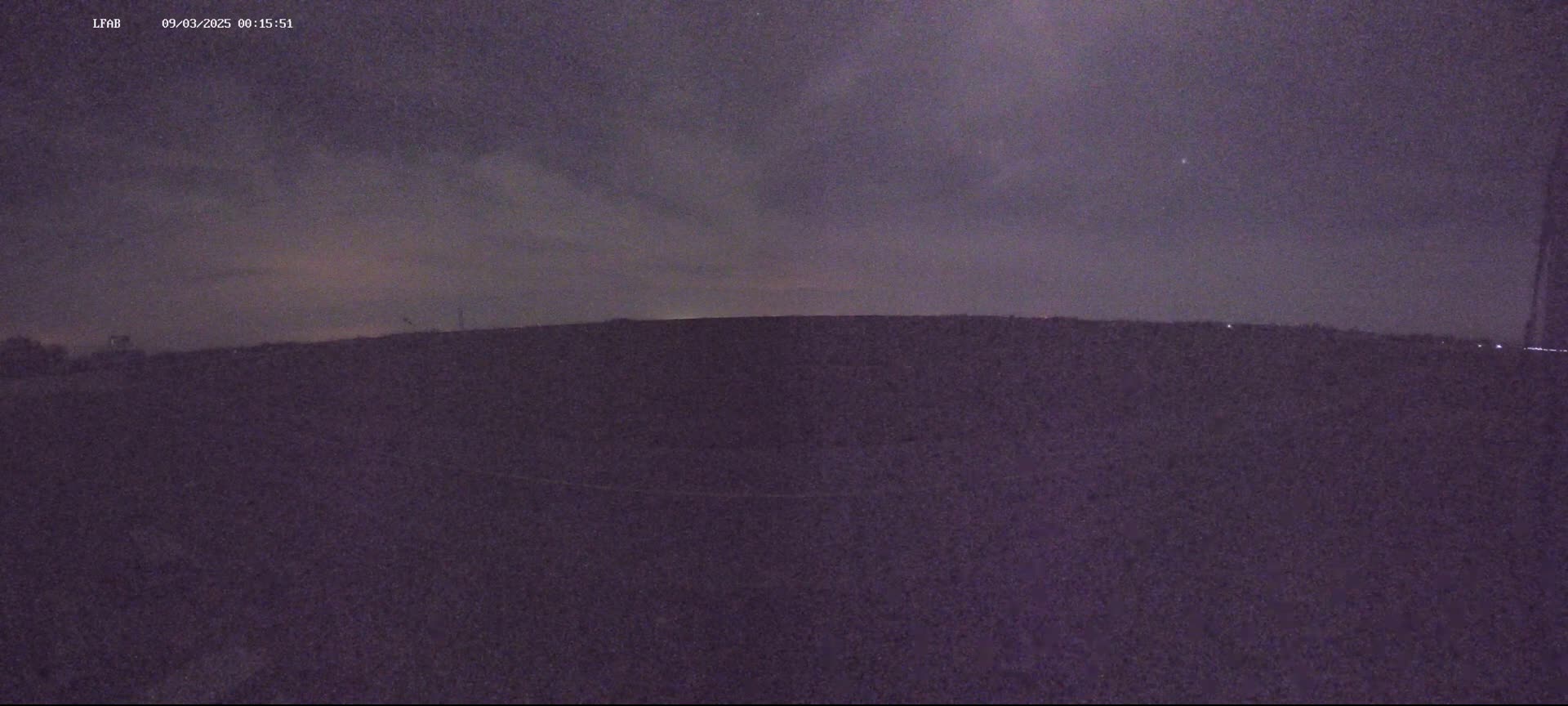 A dark, flat landscape is visible under a night sky with some clouds.