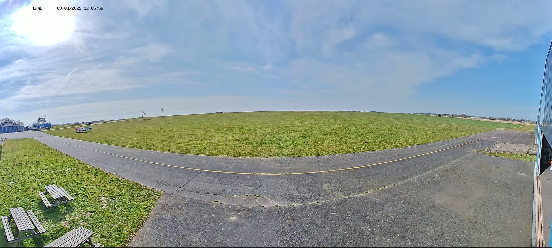 A small airplane sits on a grassy airfield under a mostly sunny sky.