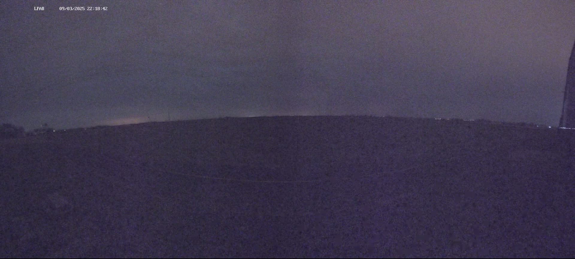 A dark, flat landscape is visible under a dusky, overcast sky at night.