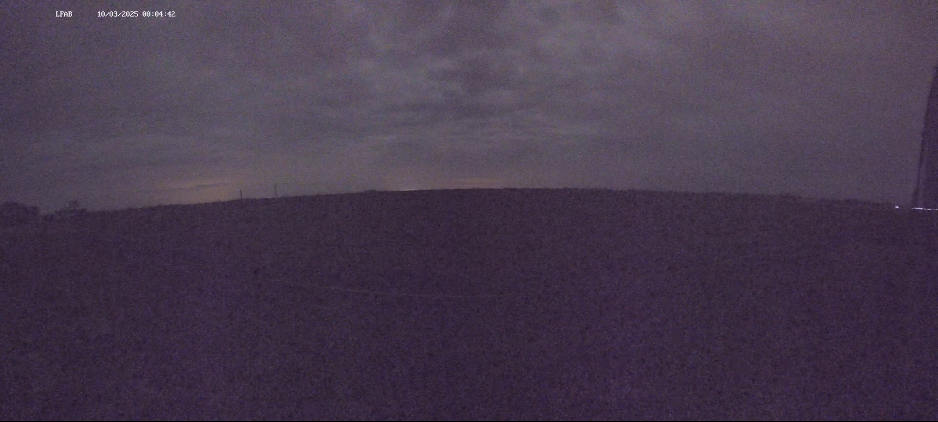 A dark, flat landscape is visible under a cloudy, nighttime sky.