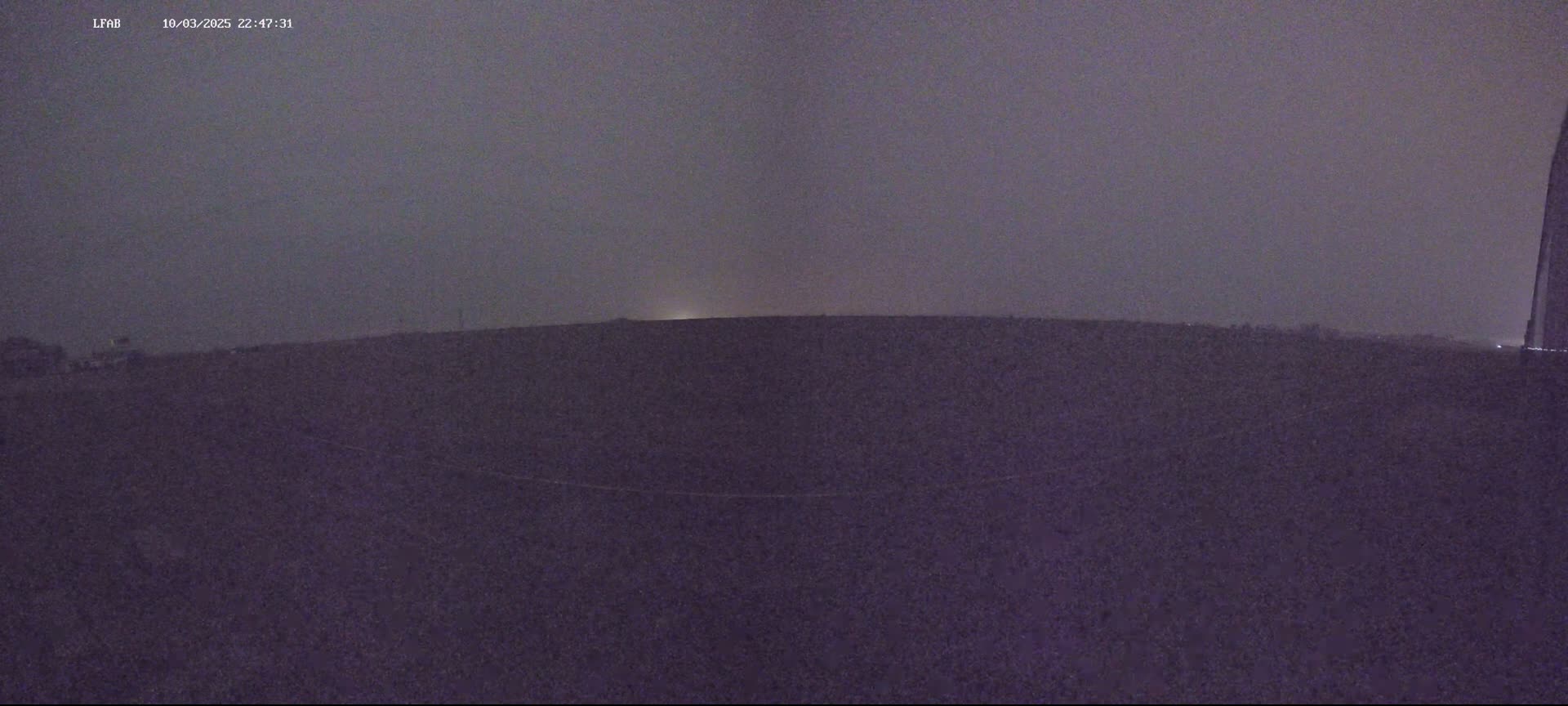 A dark, flat landscape is visible under a dusky, overcast night sky.