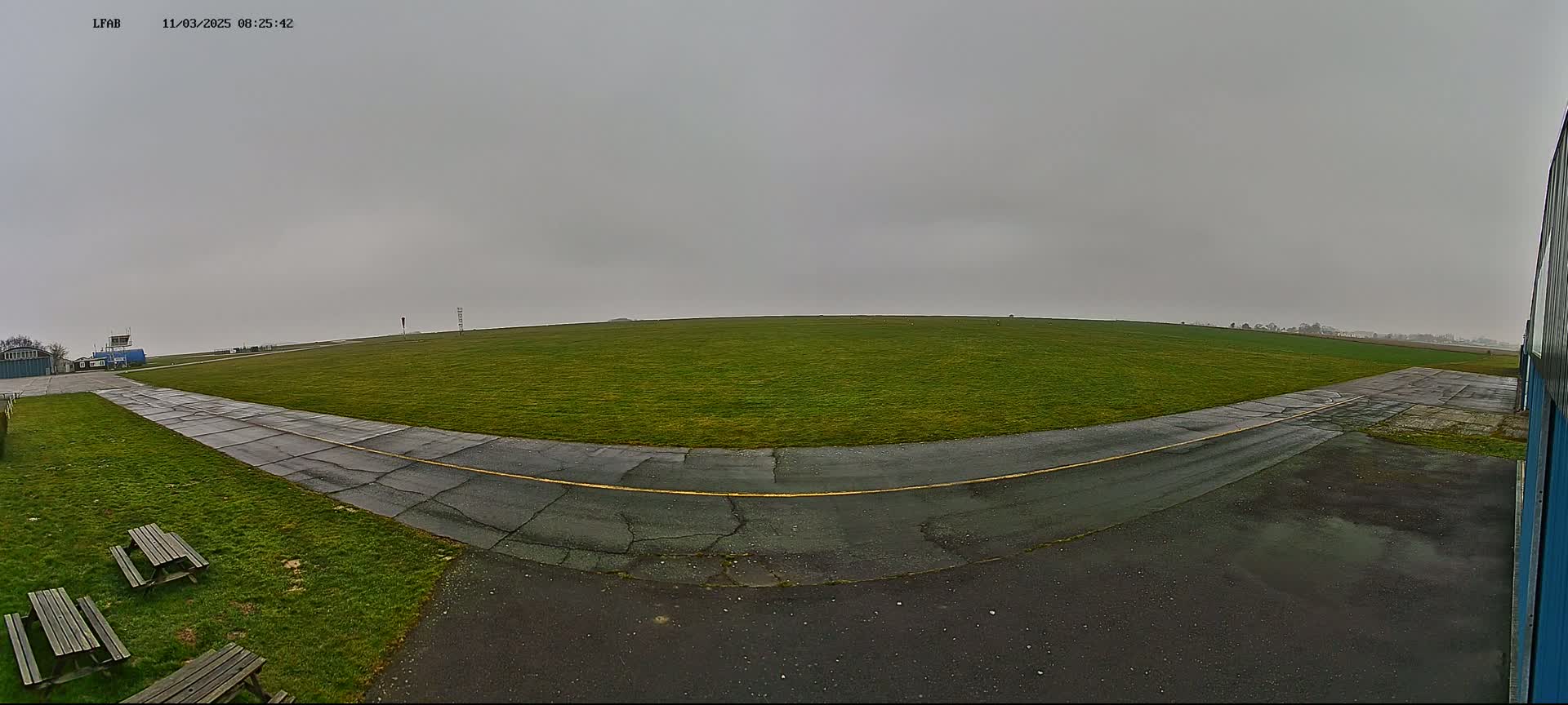 A grassy airfield with a paved taxiway is visible under an overcast sky.
