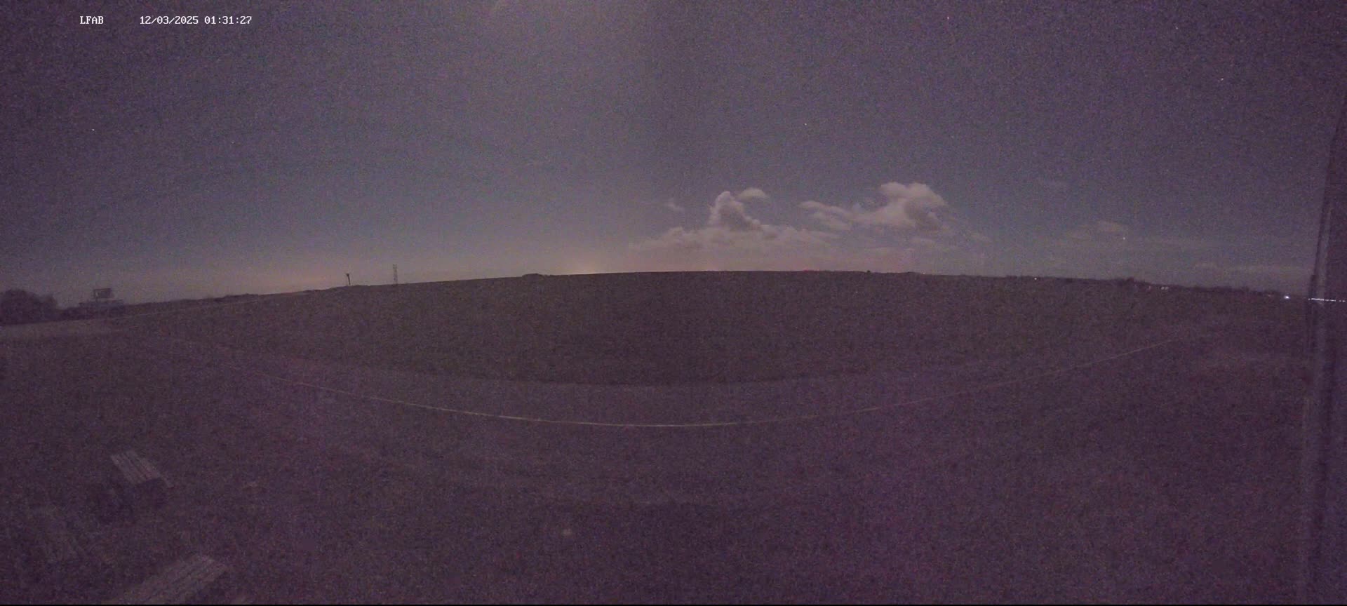 A dark, flat landscape is visible under a mostly clear night sky with a few clouds.