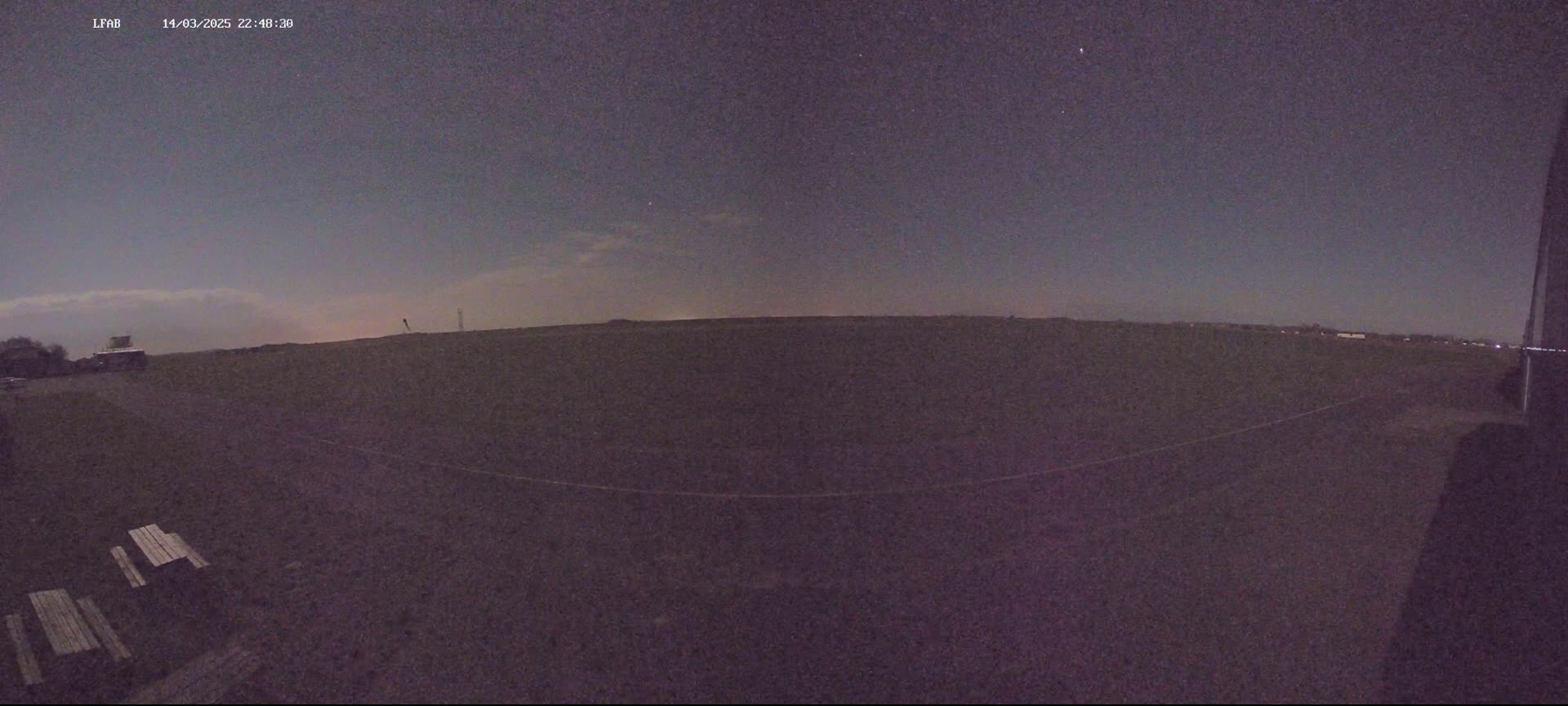 A dark, flat expanse of land is visible under a night sky with some faint clouds and stars.