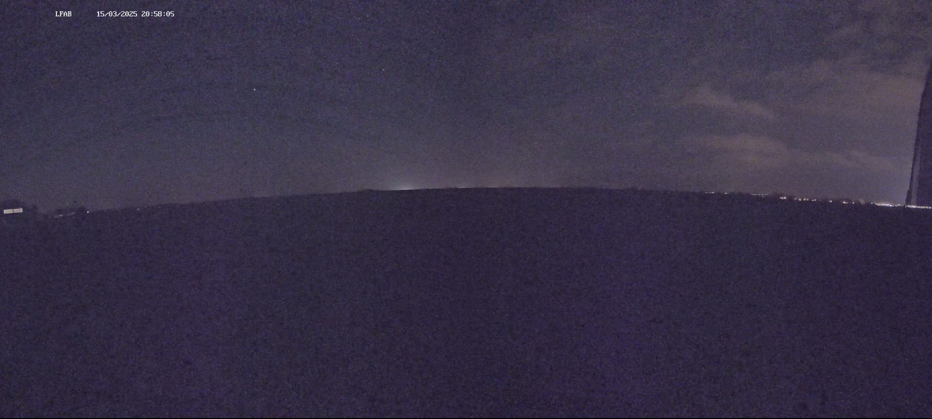 A nighttime, low-light view of a dark landscape under a partly cloudy sky.