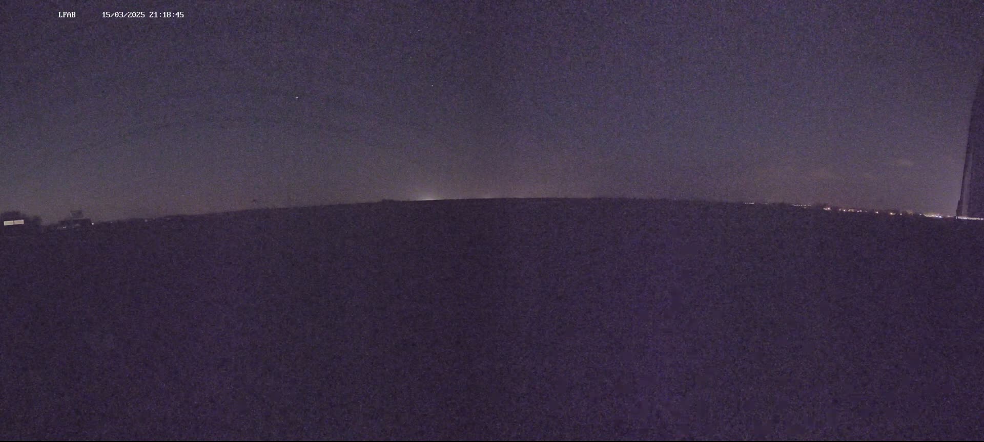 A dark, nighttime landscape is visible under a mostly clear, dark sky with a few faint stars.