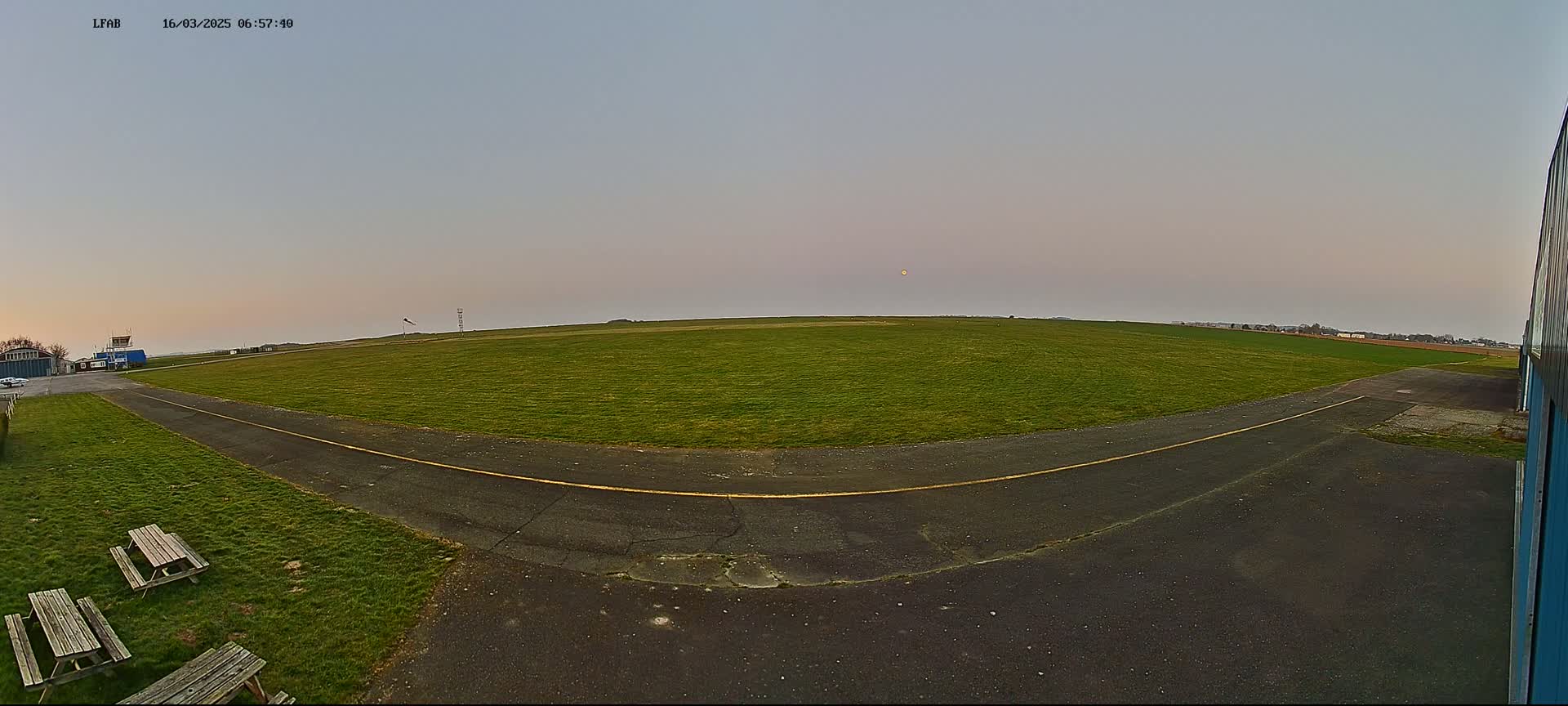A large grassy field with a paved area and picnic tables is visible under a pale, dusky sky.