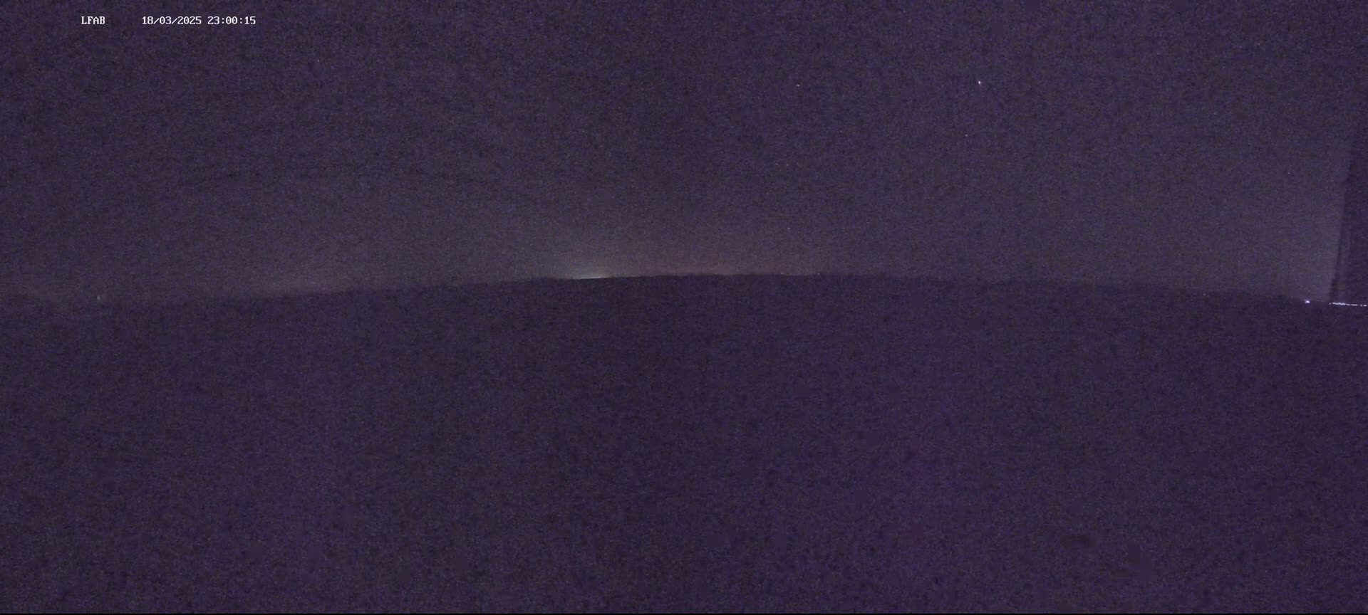 A dark, nighttime landscape shows a distant horizon line under a mostly clear, starlit sky.