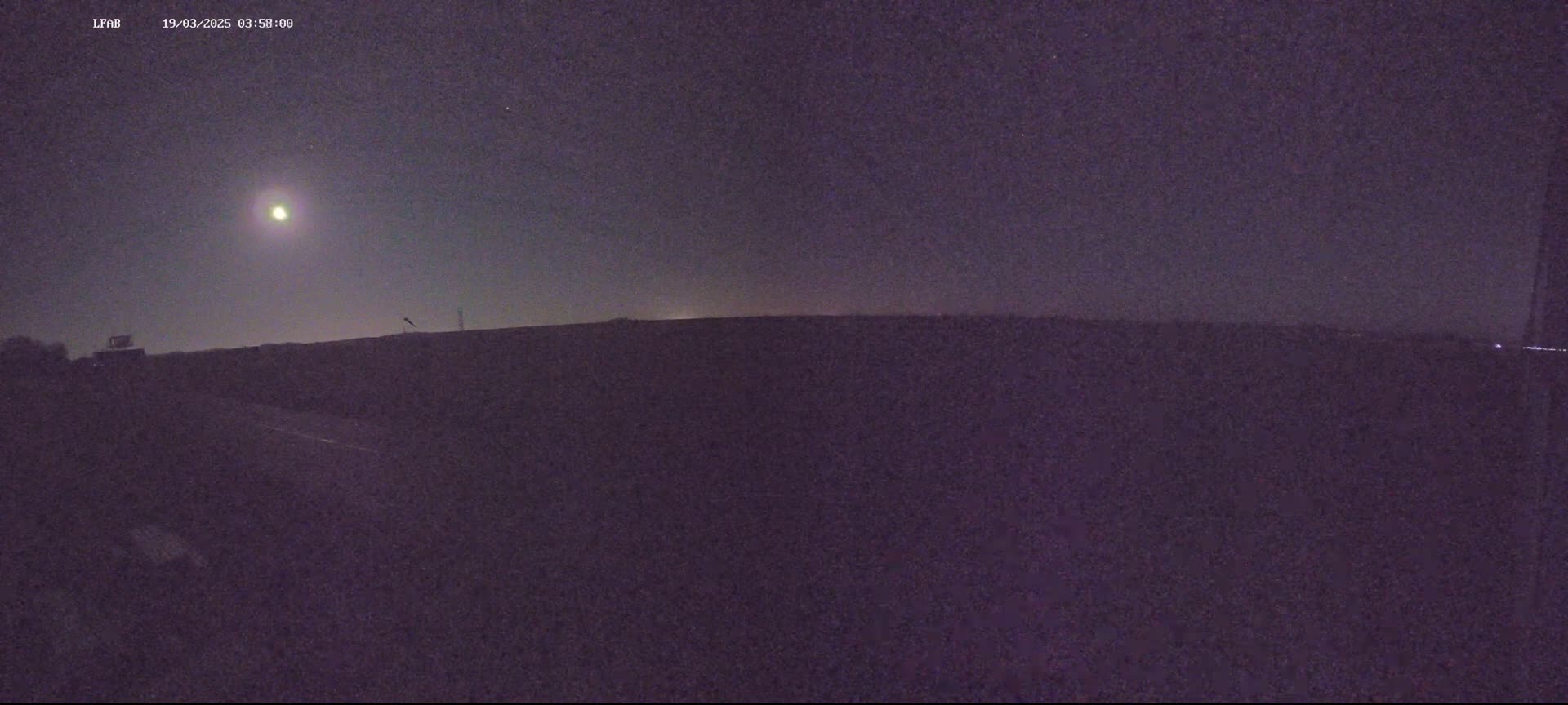 A bright moon illuminates a dark, flat landscape under a clear night sky.