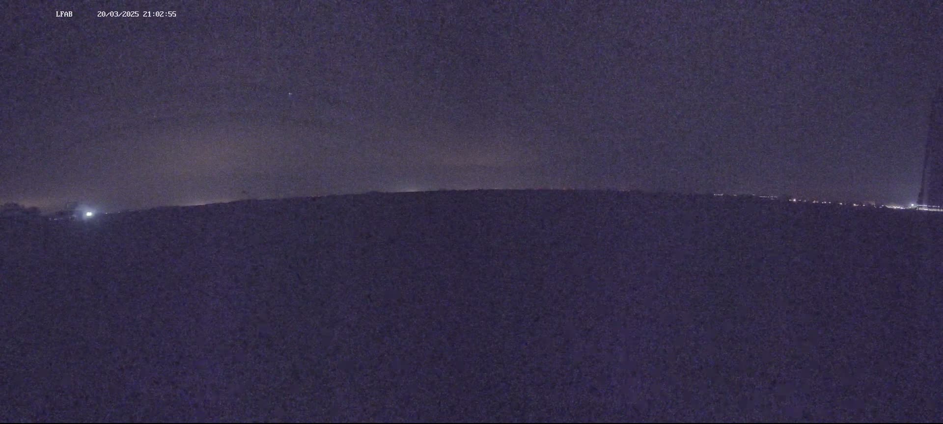 A dark, nighttime landscape is visible, with a faint horizon line and a few distant lights.