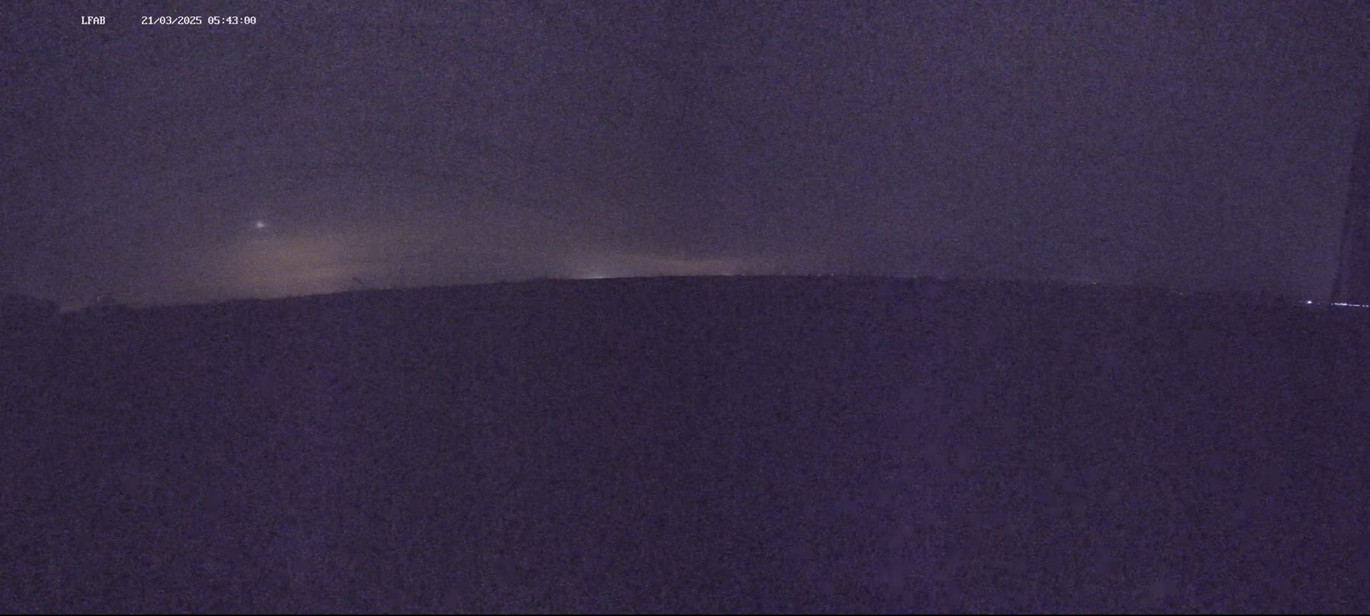 A dark, nighttime landscape shows a flat horizon line under a dusky purple sky with a faint light in the distance.
