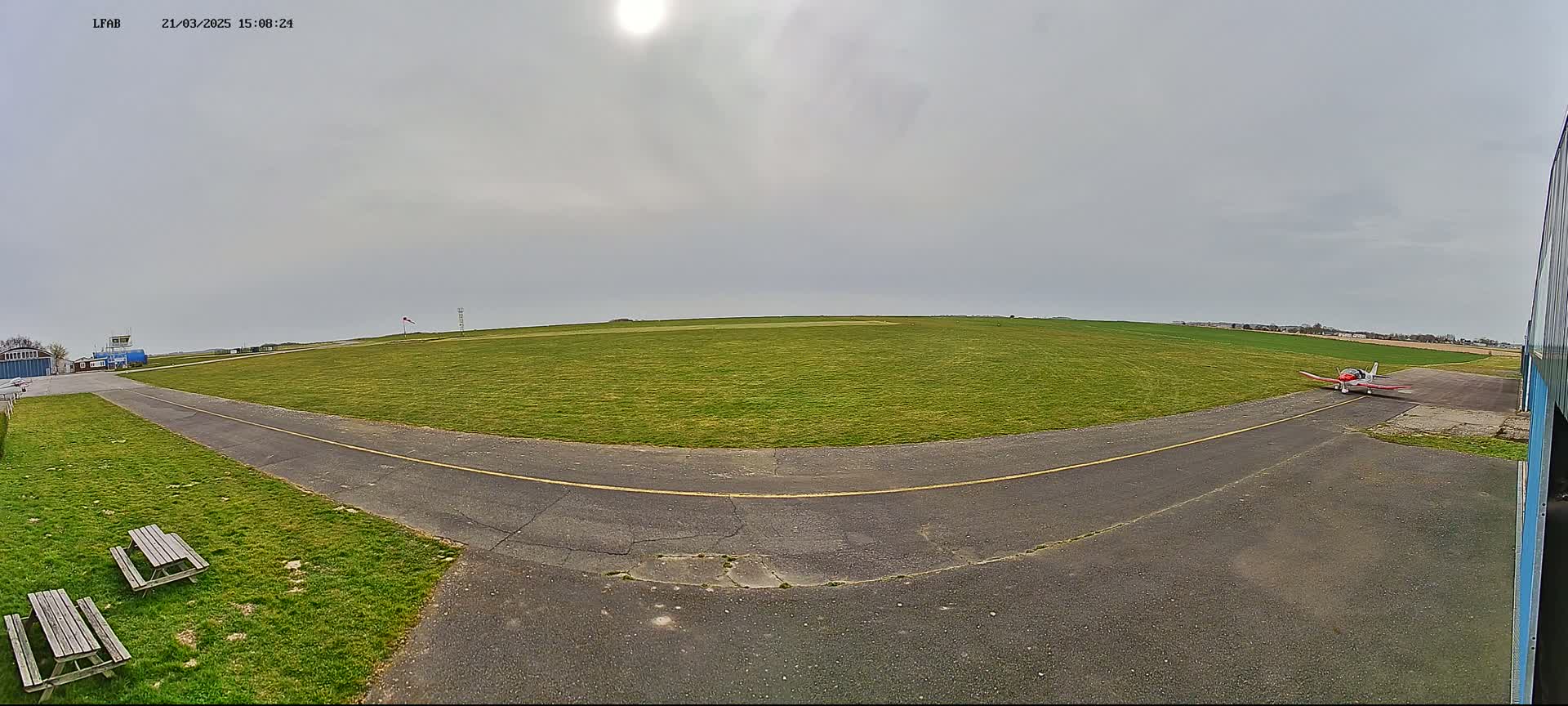 A small airplane sits on a grassy airfield under a mostly cloudy sky.