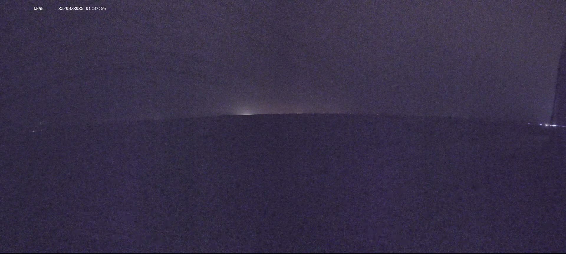 A nighttime, dark purple landscape is visible, with a faint light source on the horizon.