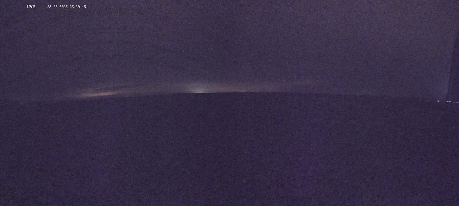 A dark, nighttime landscape is shown with a faint, bright horizon line.