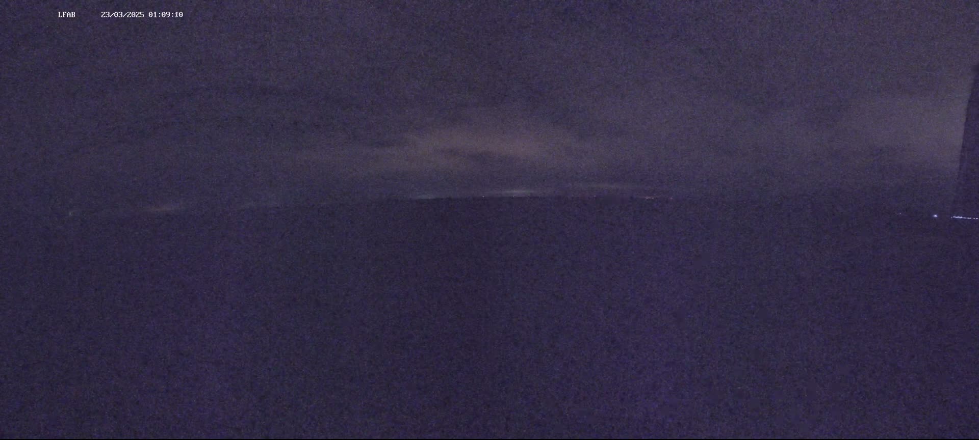 A dark, nighttime outdoor scene shows a mostly cloudy sky above a flat, dark horizon.