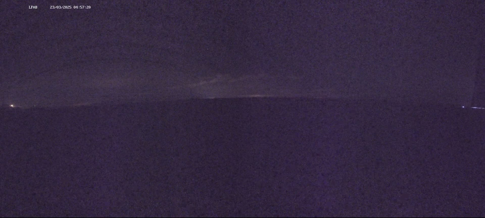 A dark, nighttime scene shows a flat, dark landscape under a cloudy sky.