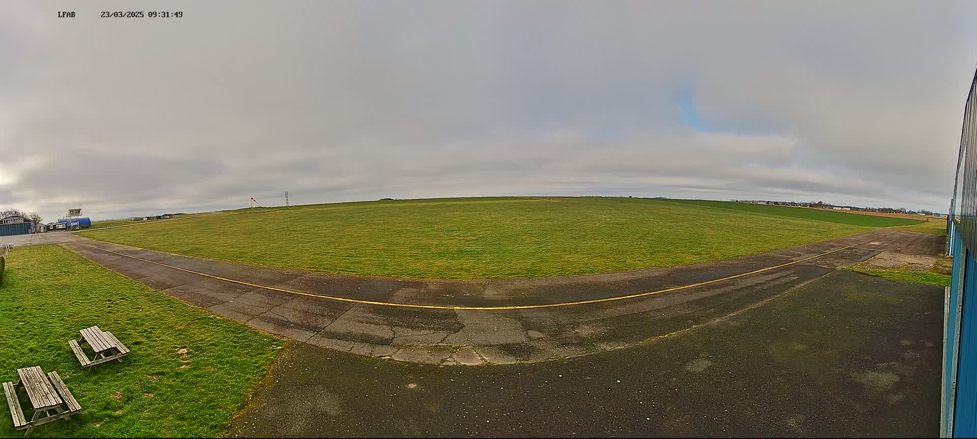 A grassy airfield with a paved taxiway is visible under an overcast sky.