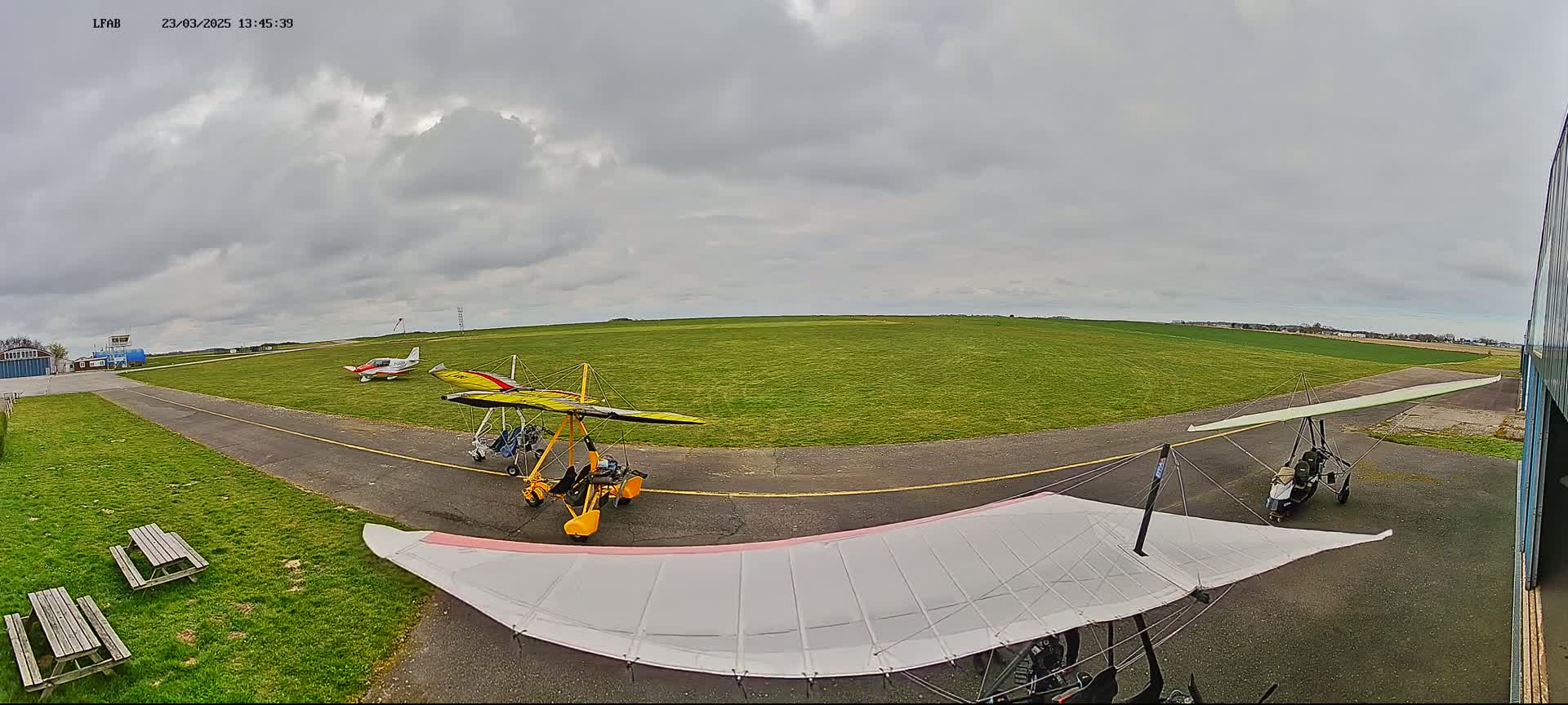 A small airfield with several light aircraft parked on a grassy tarmac under a cloudy sky.