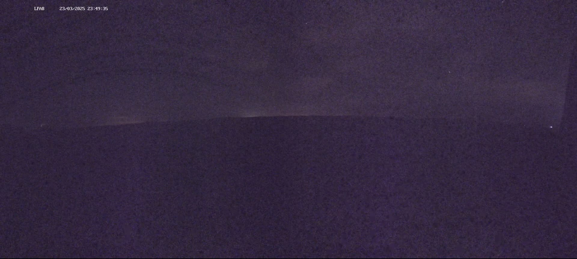 A dark, nighttime outdoor scene shows a flat, dark horizon under a mostly clear, dark sky.