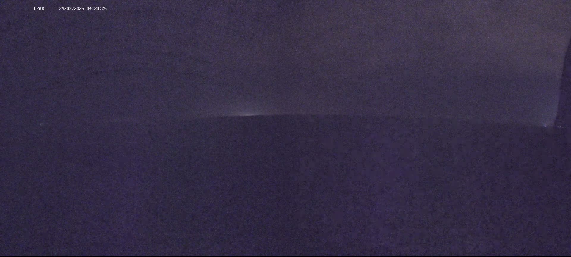A low-light nighttime image shows a dark, possibly overcast sky with a faint horizontal line of light on the horizon.