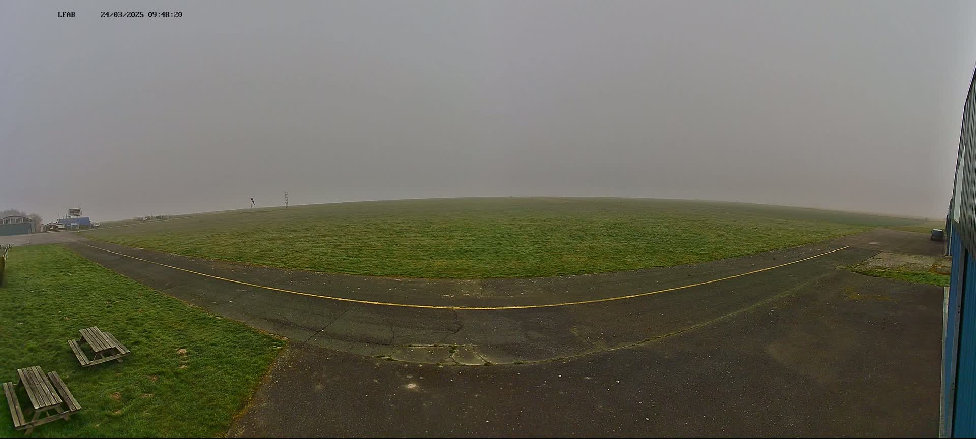 A foggy airfield with a grassy field, a paved runway, and picnic tables is visible.