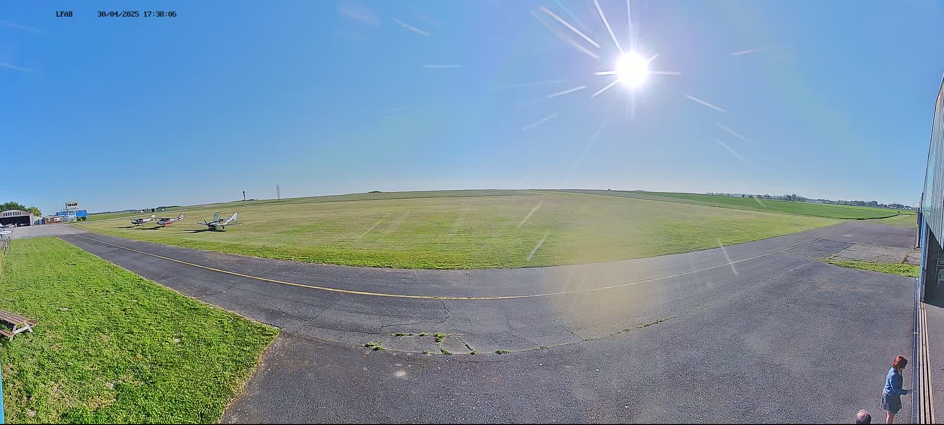 Several small airplanes are parked on a grassy airfield under a bright, sunny sky.