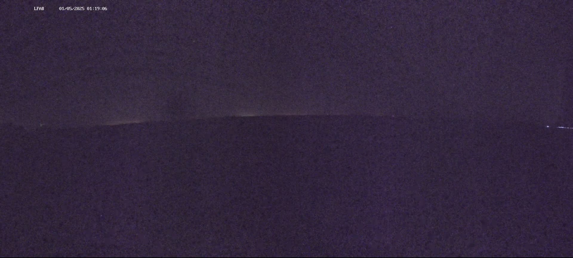 A dark, nighttime scene shows a faint, horizontal line of light on the horizon under a mostly clear, dark sky.