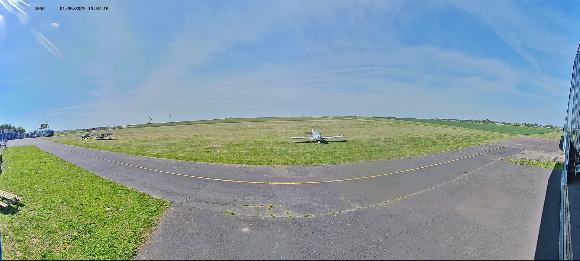 Two small airplanes sit on a grassy airfield under a mostly sunny sky.