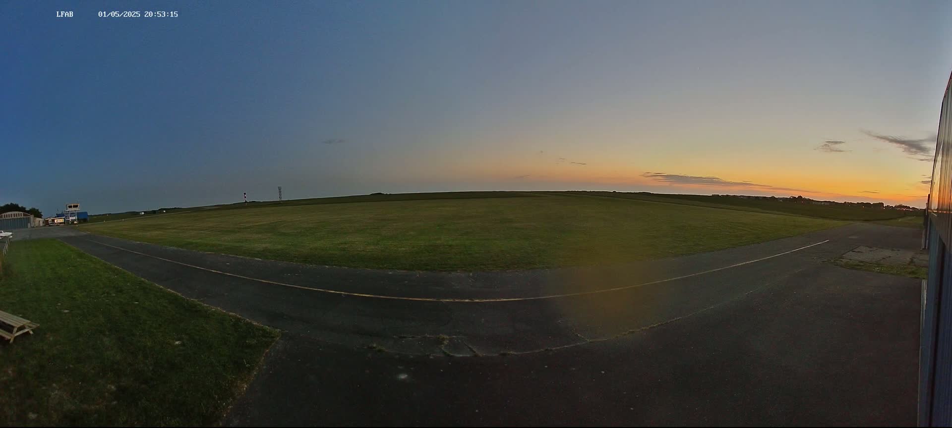 A grassy airfield with a paved taxiway is visible at sunset under a clear sky.