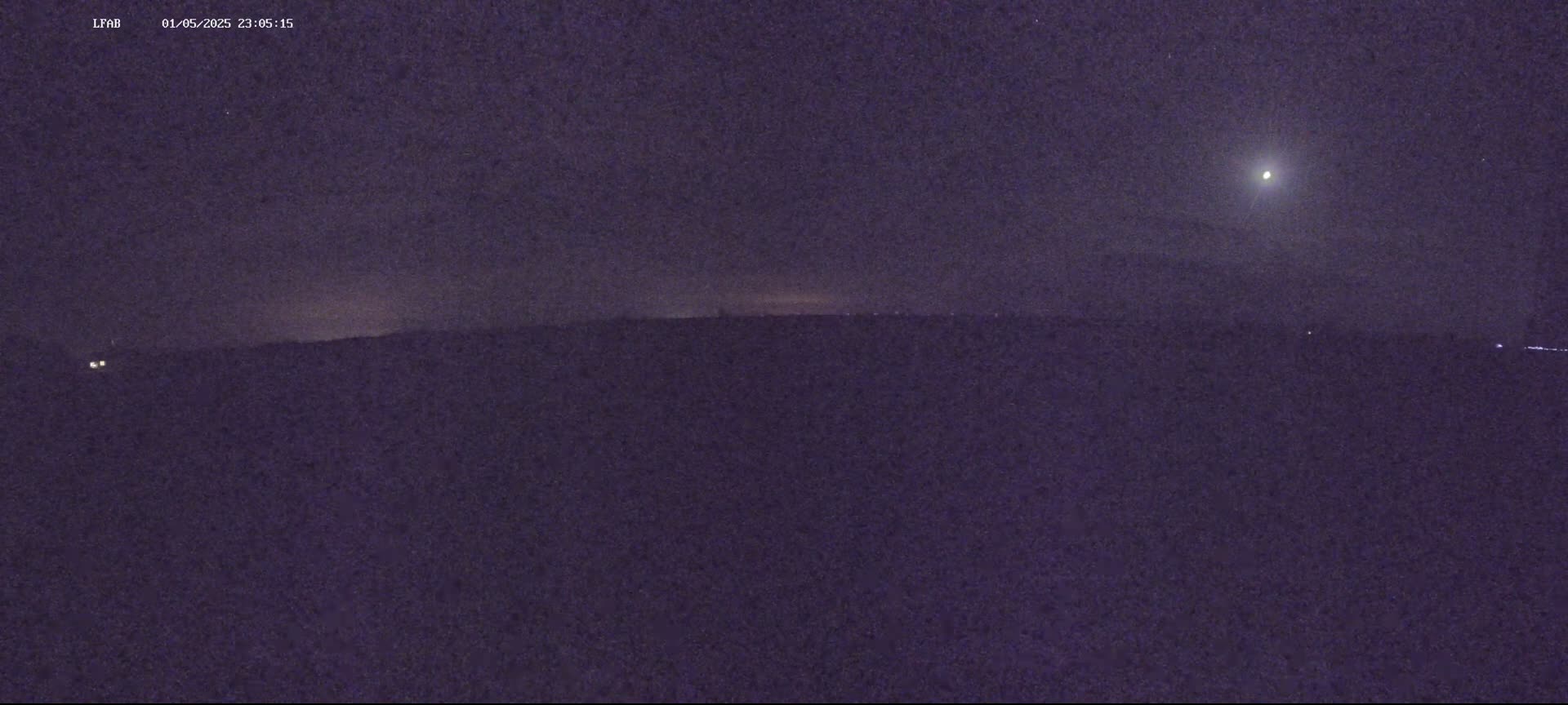 A bright light appears in a dark night sky above a dark, flat horizon.