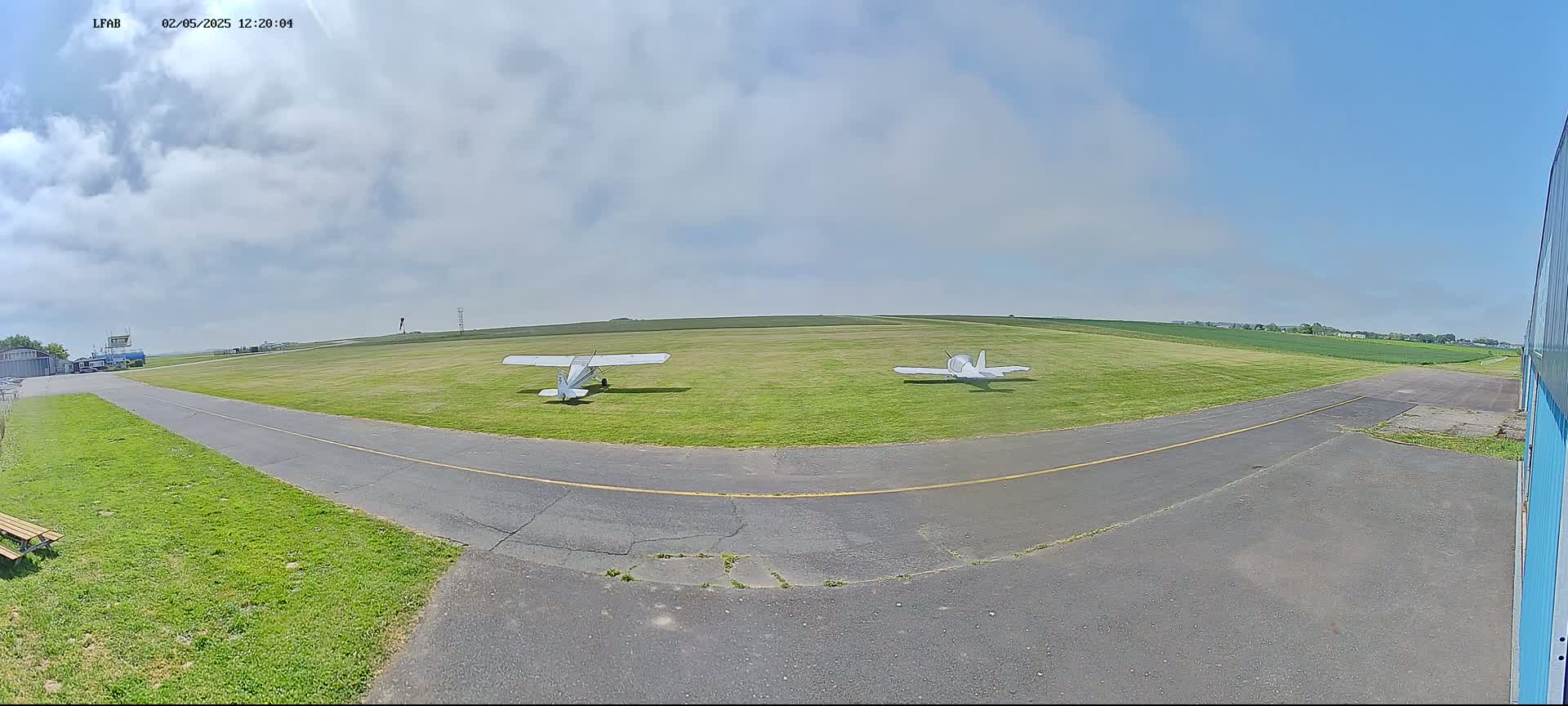 Two small airplanes sit on a grassy airfield under a partly cloudy sky.