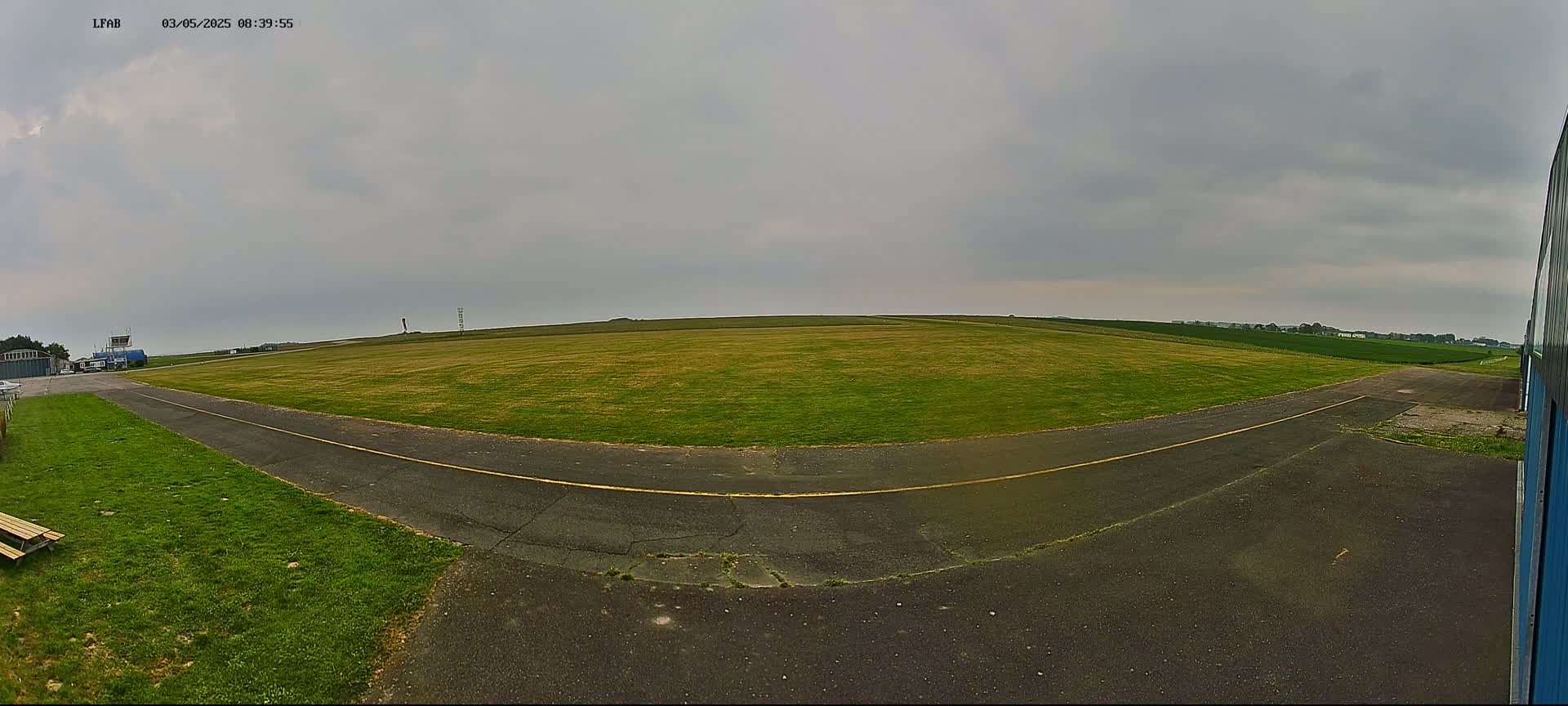 A grassy airfield with a paved taxiway under an overcast sky.